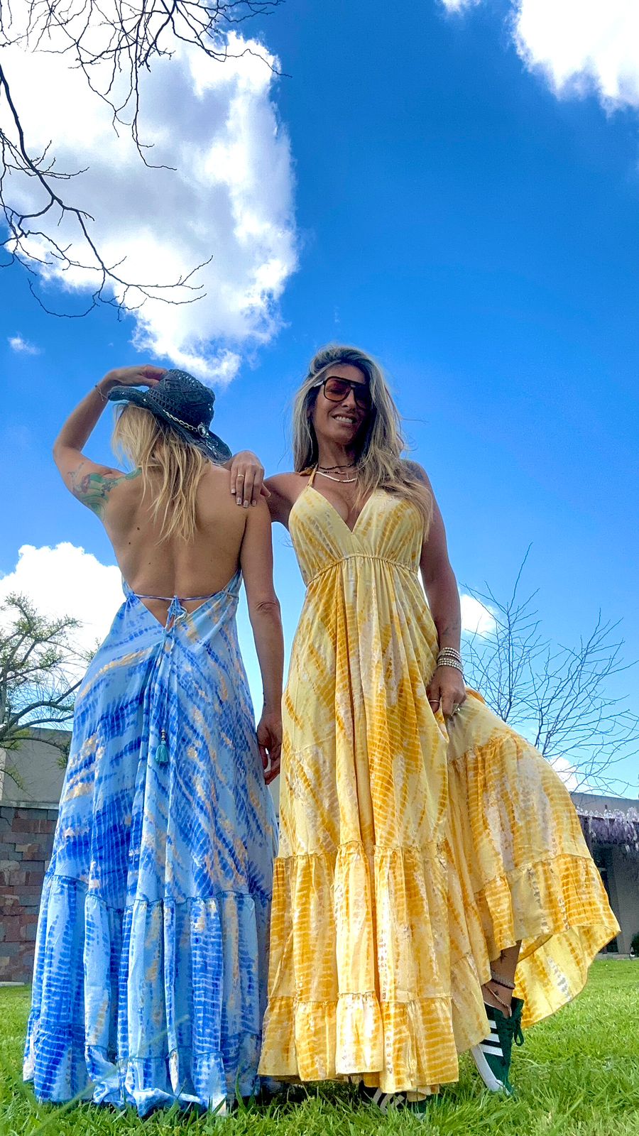Two models wearing the Nati Dress one in blue silk maxi with front view, and one in gold silk maxi showing the open back
