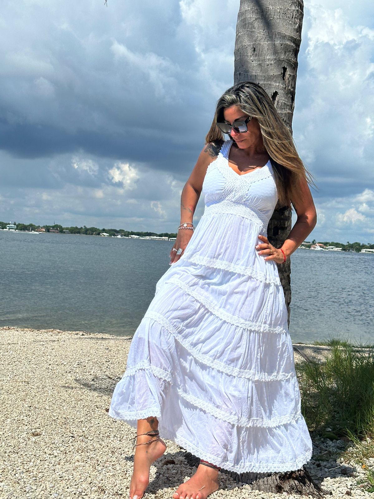 Model leaning on a palm tree wearing the Ruby Dress, a long white cotton maxi dress, ideal for resort and summer style