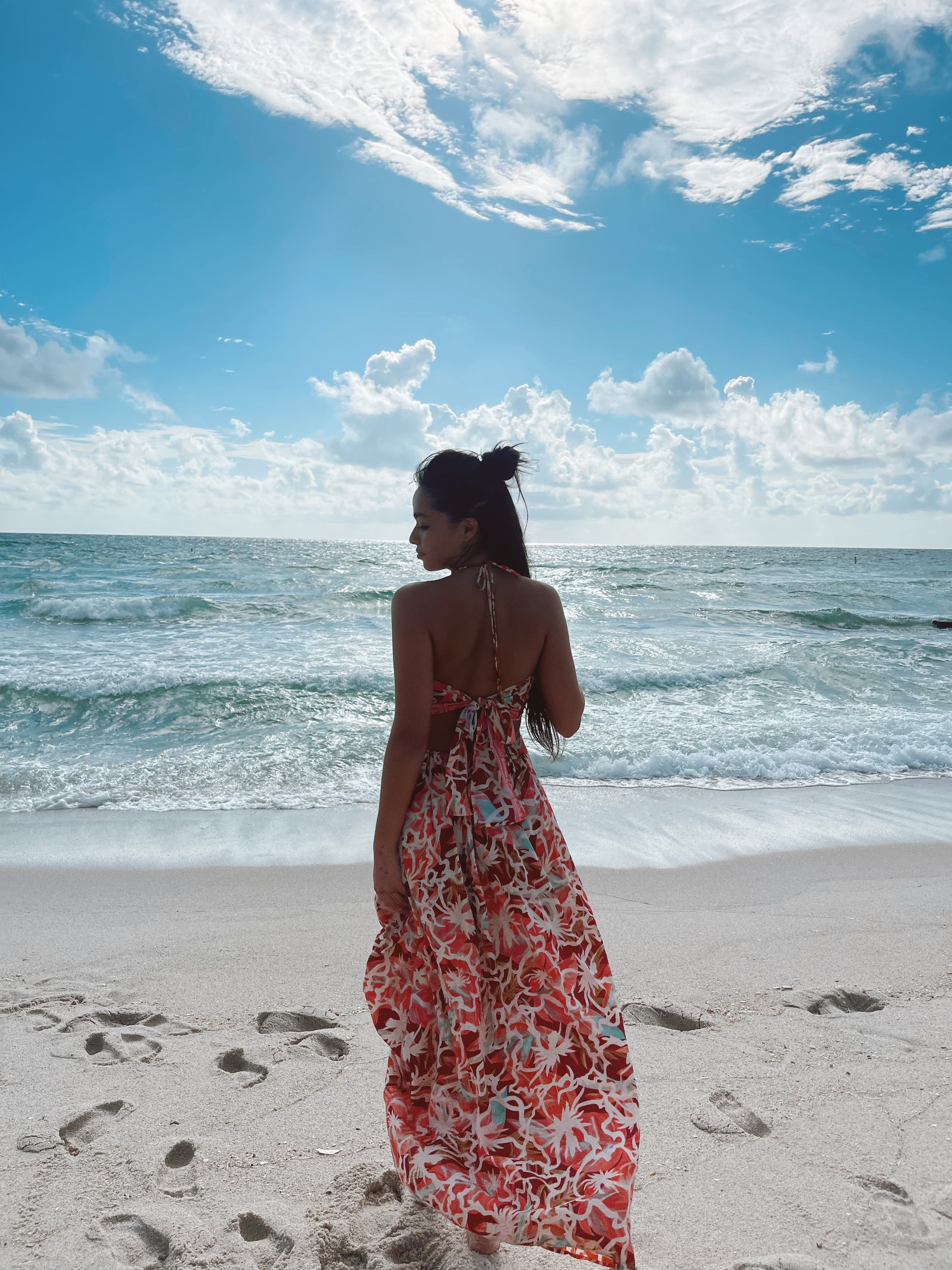 Back view of model at the beach wearing a multicolor silk maxi dress with open back tie